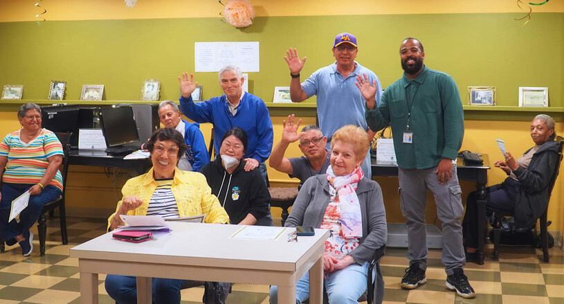 group of seniors sitting at a table waving at the st. barnabas senior center